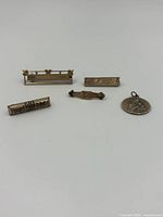 Five brass pins arranged on a white surface showing different shapes and decorations