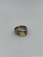 Close-up side view of a bold band ring showing a brushed sterling silver surface with a shiny gold rectangular accent on top.