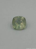 Light greenish iolite gemstone, princess cut, shown on a neutral background with script watermark.