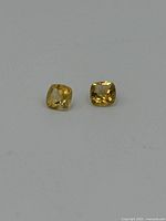Two yellowish cushion cut gemstones lying flat on white background showing their table facets.