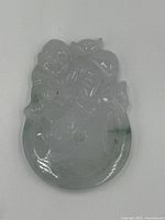 Front view of the carved jade pendant showing detailed carving and light green color with darker green inclusions.