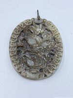 Front view of the jade pendant showing detailed dragon carving with textured surface and metal loop attachment.