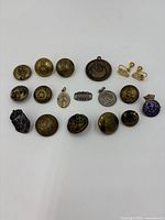 Overview of all 18 brass and silver buttons and pins arranged together, showing a variety of sizes and styles.
