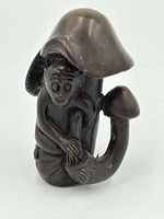 Front view of dark polished netsuke showing monkey holding mushroom with clear facial and textural details.