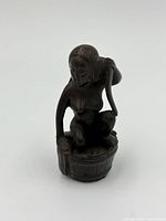 Front angle view of the small carved figure depicting a woman in a tub holding a towel over her shoulder.