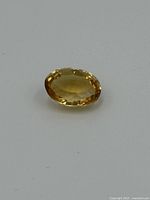 Oval faceted citrine gemstone on a white background that shows its golden yellow color and clarity.