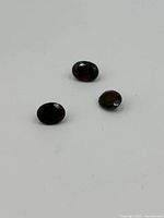 Three dark oval cut opal gemstones photographed on white surface.