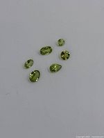 Six loose peridot gemstones of various sizes and shapes on a white background for color and clarity display.
