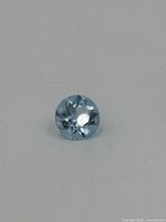 Clear top-down view of the round cut blue topaz gemstone showing brilliant faceting and medium light blue color.