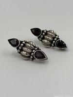 Pair of sterling silver earrings with deep red pear-shaped ruby stones laid on white surface showing front detail.