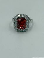 Front view of ring showing rectangular orange-red sapphire center surrounded by clear baguette-cut stones on a sterling silver band.