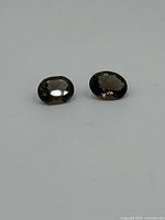 Pair of oval cut smoked quartz gemstones with brown translucent color on a white background.