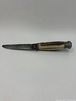 Side view of the knife showing the serrated blade and bone handle with metal end caps.