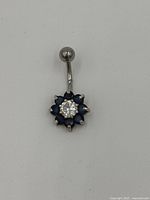 Sterling silver belly button ring with flower motif consisting of blue sapphire stones surrounding a clear cubic zirconia center stone.
