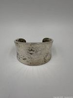 Front view of a wide sterling silver cuff bracelet showing hammered texture and tarnish.