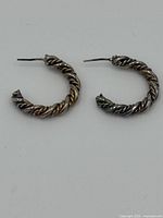 Pair of twisted sterling silver half hoop earrings shown on plain white background.