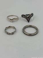 Four sterling silver rings arranged on white background showing different styles and sizes.