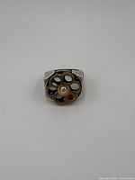 Top view of the sterling silver ring showing the spinning bullet casing with six holes, central raised circle, and red gem.