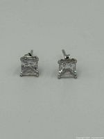 Pair of sterling silver stud earrings with clear square stones laid flat on white surface.