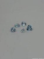 Five light blue topaz gemstones displayed on white background, showing multiple shapes and facets.