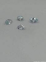 Four faceted light blue topaz gemstones shown on a white surface, clearly displaying their cuts and clarity.