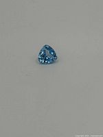 Clear close-up of a small trilliant-cut blue topaz gemstone against a light background.