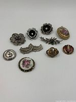 Overview of 10 vintage brooches arranged on a white background showing various floral and decorative styles.