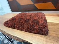Angled view of thick dark red wool mat showing texture