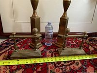 Front and rear pairs of brass andirons with tape measure and water bottle for scale