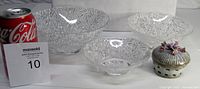 Three clear cut Mikasa crystal bowls with intricate leaf patterns and a small decorative porcelain Capodimonte trinket box with floral design on lid, all displayed beside a Coke can for size reference.