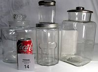 Photo showing four clear glass jars with differing shapes and metal or glass lids, with a Coca-Cola can for scale and lot number card in front.