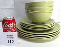 Stack of 12 avocado green ceramic dishes including dinner plates, salad plates, and soup bowls, with a soda can for scale