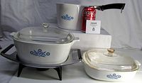 Photo shows all three Corningware pieces: sauce maker, two casserole dishes with lids, plus warming tray and a Coca-Cola can for size reference.