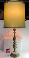 Full view of the urn-style table lamp lit with pale green cylindrical fabric shade, standing on white pedestal with a soda can beside for scale, showing approximately 36 inch height and detailed painted and cast iron base.
