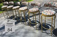 Full view of six ISA International swivel bar stools arranged on driveway showing colorful Jacquard upholstery and gold metal frames.
