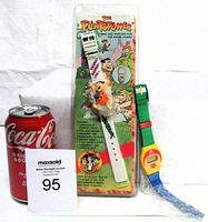 Two novelty watches side-by-side for scale with Coca-Cola can; Flintstones watch in original packaging and colorful Dairy Queen watch out of package.