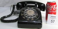 Front view of black Northern Electric rotary phone next to a soda can and lot number card, showing dial and handset