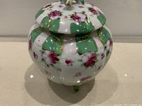 Front view of footed porcelain jar with lid showing green panels, pink flowers, gilt trim