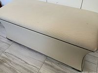 Full side view of cream upholstered bench showing nailhead trim