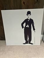 Front view of unframed black and white canvas portrait of Charlie Chaplin standing with cane, minimalist silhouette style.