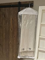 Two beige grommet drapery panels hanging covered in protective plastic bag, showing length and folded style.