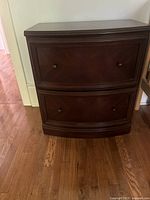 Front view of dark brown wooden filing cabinet with two drawers and round metal knobs.