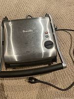 Top view of Breville stainless steel panini press showing control knob, indicator lights, and power cord with minor scratches on surface.