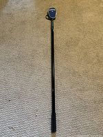 Full length golf ball retriever laid on carpet showing black metal shaft and Callaway grip.