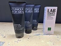 Three tubes of Clinique for Men Charcoal Face Wash and one box of Lab Series Cooling Shave Cream on a distressed surface.