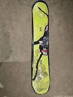 Top view of the Flow Era snowboard showing vibrant yellow and black graphics in good used condition on a beige carpet.
