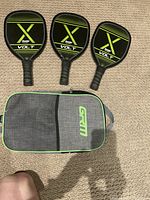Three Franklin Volt pickleball paddles arranged side by side on carpeted floor with black and green design on paddle faces and black grips. Carry case placed below paddles.