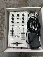Top view of white iRig Mix stereo DJ mixer with volume and tone control knobs, sliders, power indicator, and connecting cables packed in a white box.