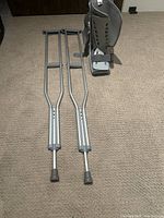 Pair of gray Guardian brand adjustable aluminum crutches and Aircast large walking boot on beige carpet