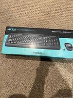 Front view of Logitech MK320 wireless keyboard and mouse combo box on carpet, showing product image and branding.